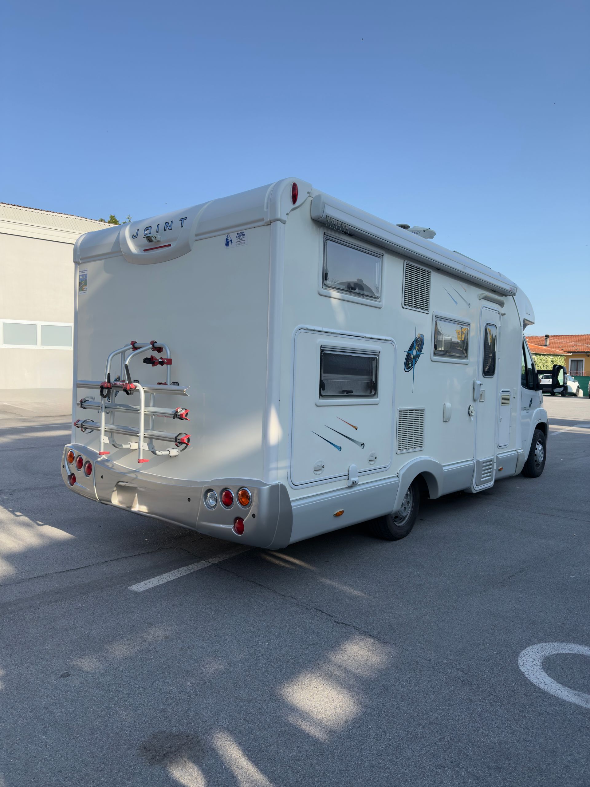 Camper bianco parcheggiato sull'asfalto, vista posteriore. Include portabici, finestrini e finiture argentate.