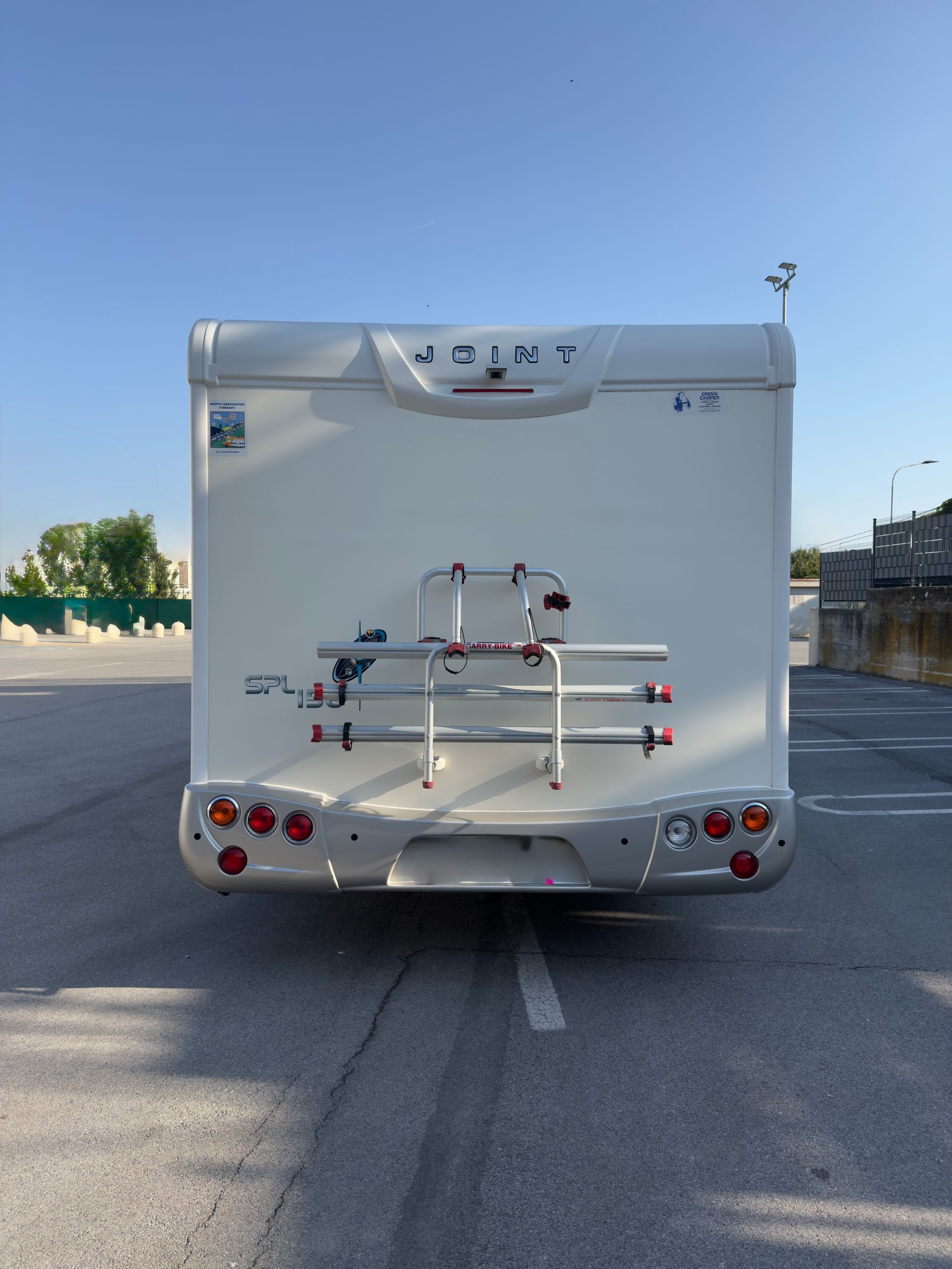 Retro di un camper bianco con portabiciclette, parcheggiato sull'asfalto.