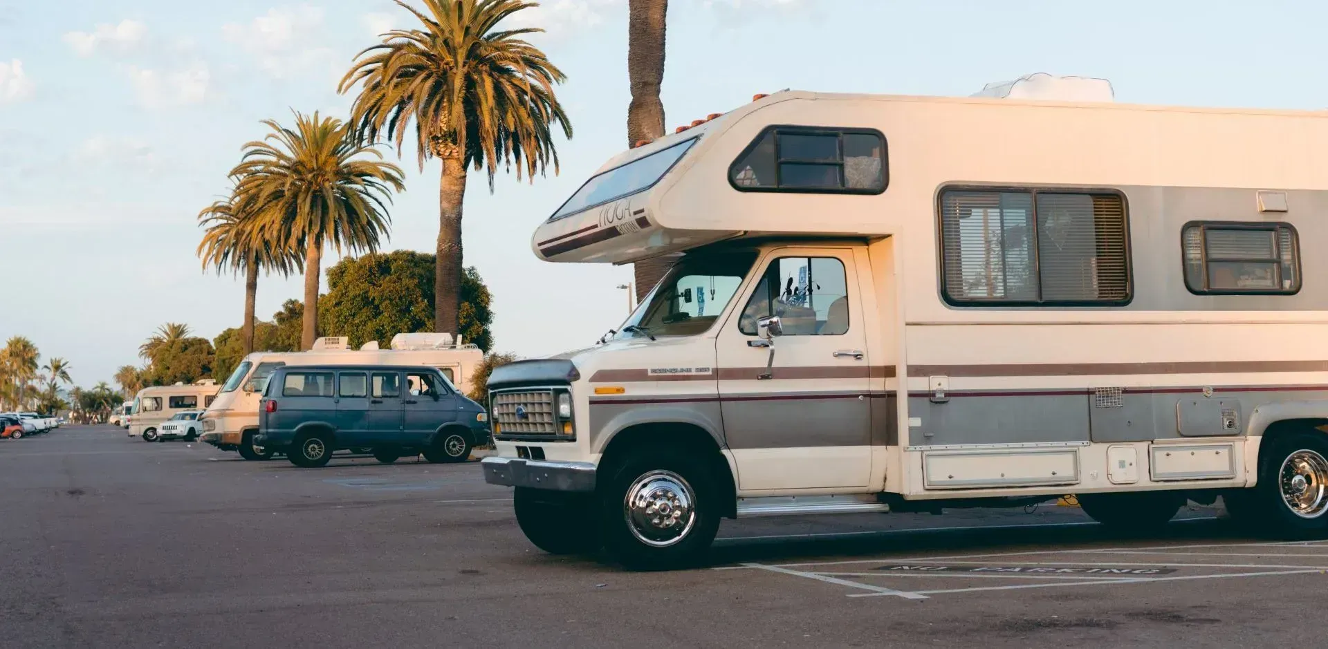 Un camper è parcheggiato in un parcheggio con delle palme sullo sfondo.