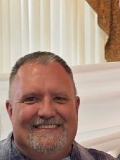 Man with short dark hair and beard smiles.