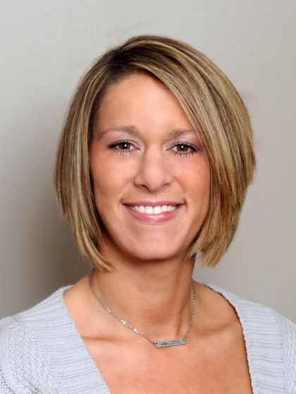 Blonde woman with short hair smiles, wearing a light gray sweater and silver necklace.