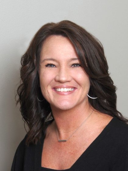 Woman with dark hair, smiling, wearing a black top, against a gray background.
