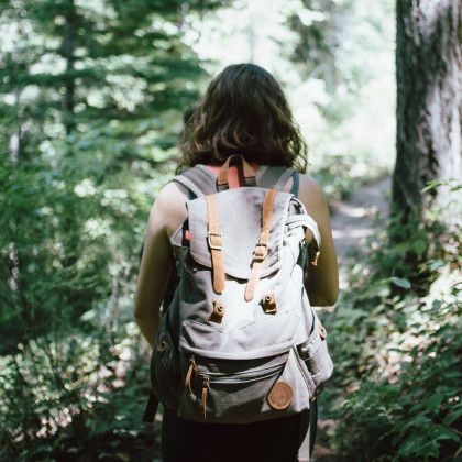 Woman hikes on a forest trail, seen from behind, with backpack.