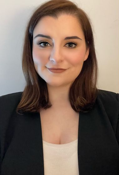 Woman with brown hair in a black blazer smiles at the camera.