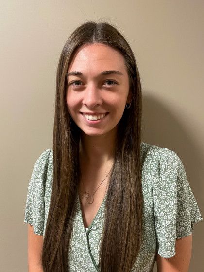 Young woman with long brown hair smiling, wearing a green floral top.