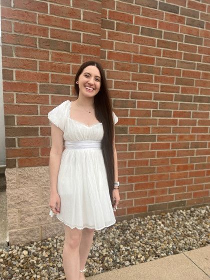 Woman in white dress smiles in front of a brick wall.