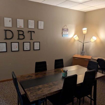 A DBT therapy room with a long table, chairs, posters, and a lamp.