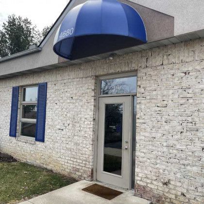 Exterior of a building with a blue awning over the door, a window with blue shutters, and a light brick facade.