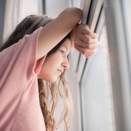 Girl with long hair resting head on arm, gazing pensively out a window.
