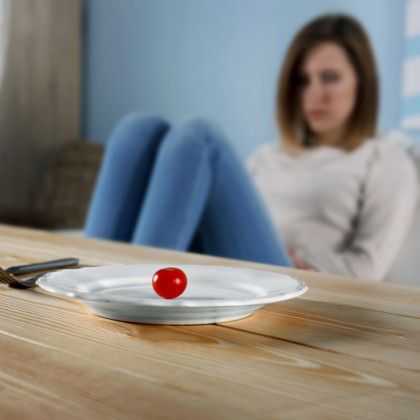A single cherry tomato on a plate; sad woman in background.