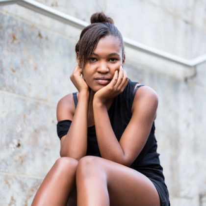 Woman sitting on steps, wearing black, resting her chin on hands, looking at the camera.