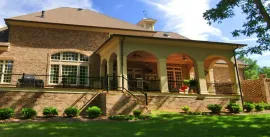Large brick house with arched porch, green lawn, and clear blue sky