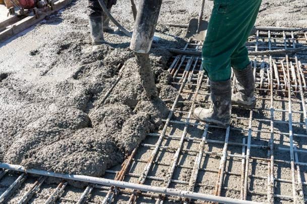 Construction workers pouring wet concrete over a steel reinforcement grid during slab construction. 