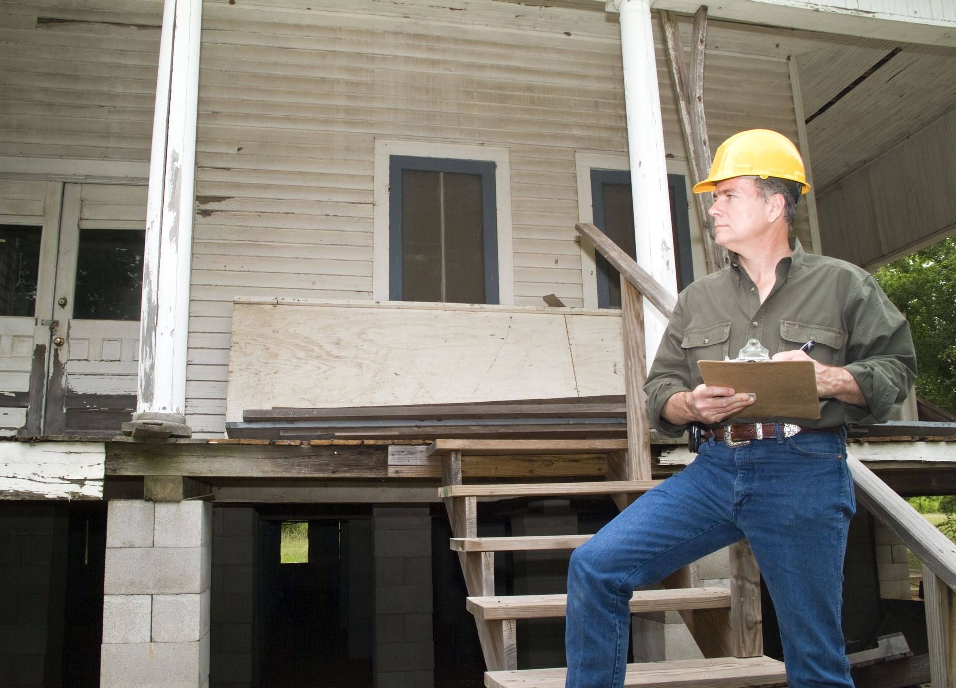 A man wearing a hard hat holds a clipboard in front of a house