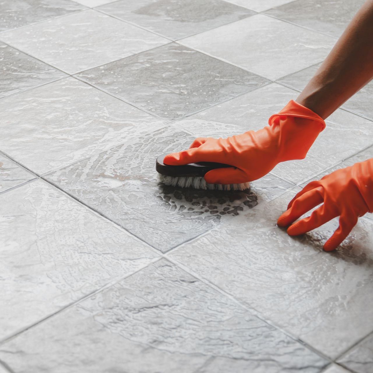 a person wearing orange gloves is cleaning a tiled floor