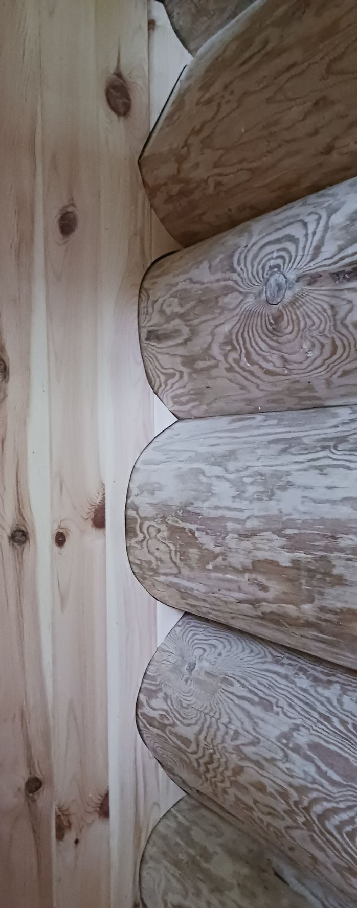A vertical view of a corner where smooth, knotty light wood panels meet rounded, textured log walls.