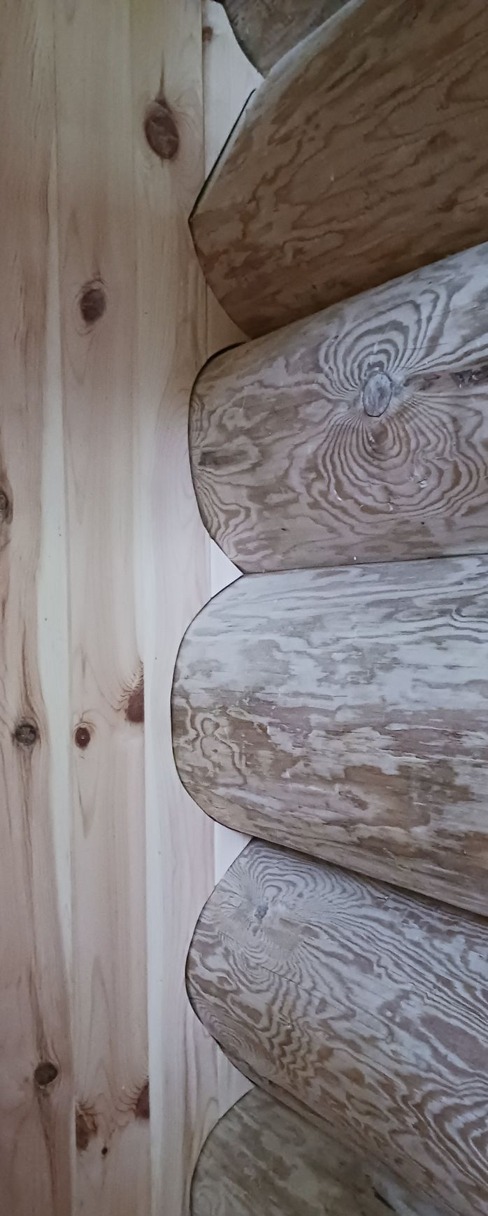 A vertical view showing the meeting point between a flat, light-colored pine wall and a textured, stacked log corner wall.