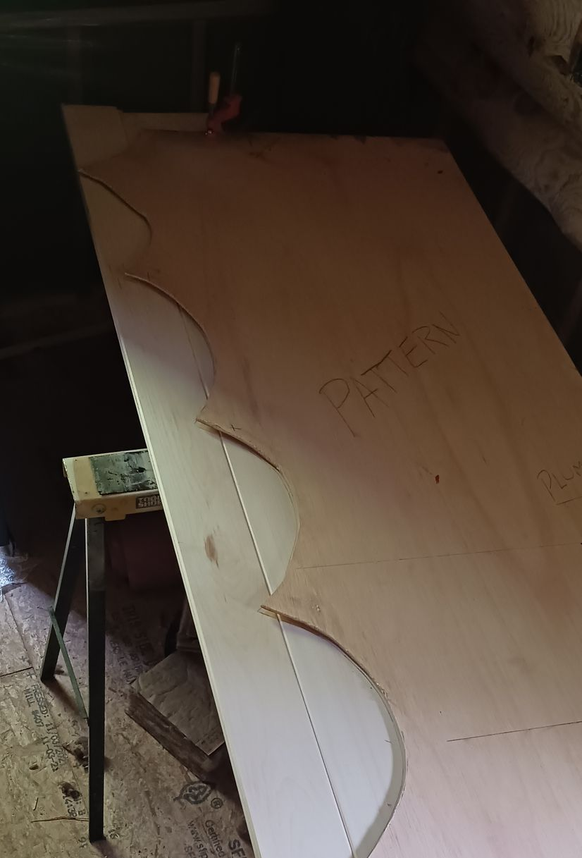 A large wooden board rests on a sawhorse, marked with a hand-drawn scalloped design pattern for cutting.