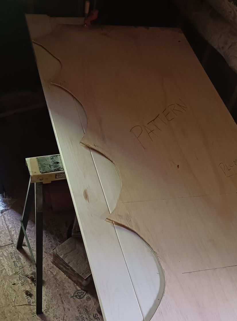 A large wooden board rests on a sawhorse, marked with a hand-drawn scalloped design pattern for cutting.