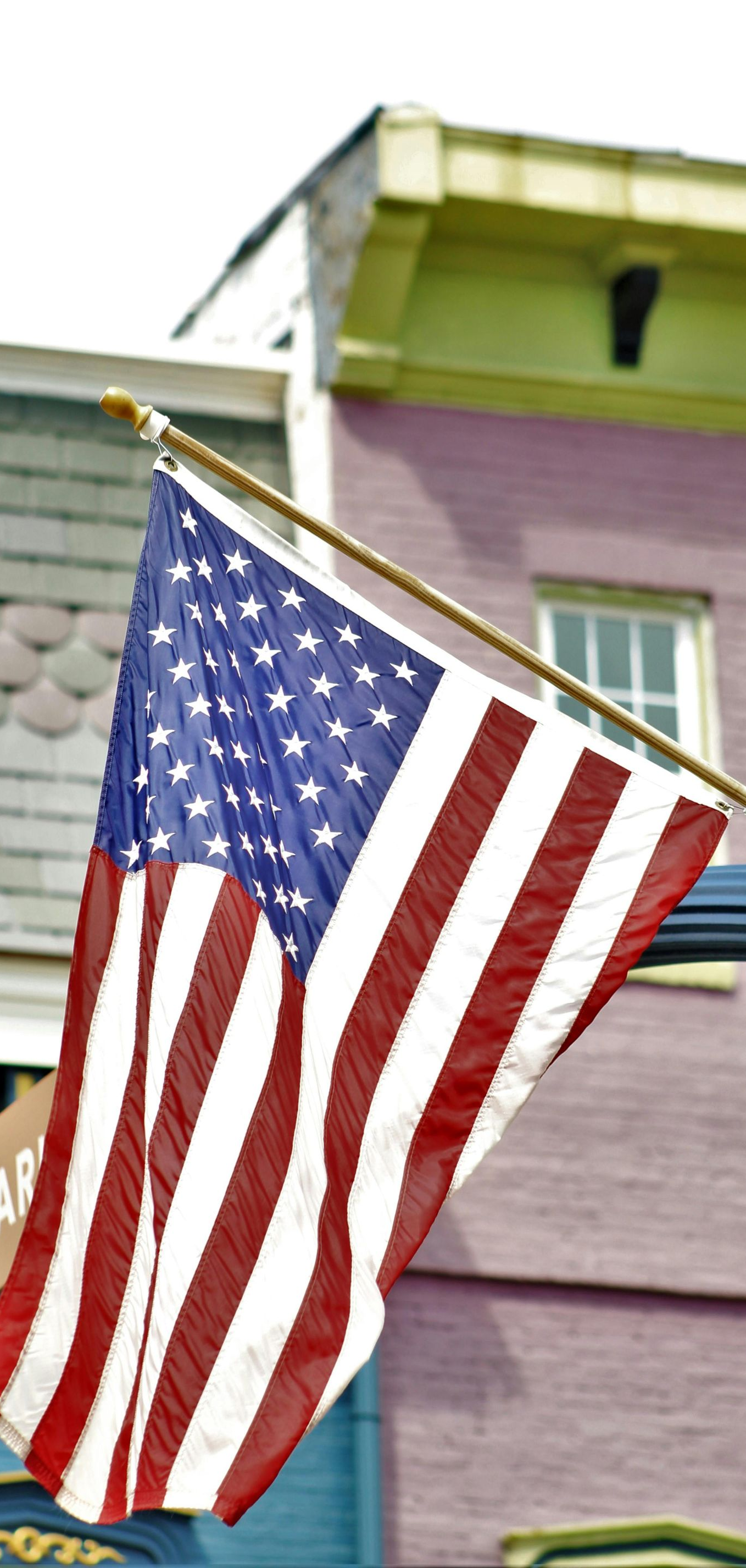 A US flag hangs on a pole against a backdrop of colorful, historic-style brick building facades.
