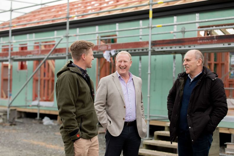 Three men are standing in front of a building under construction.