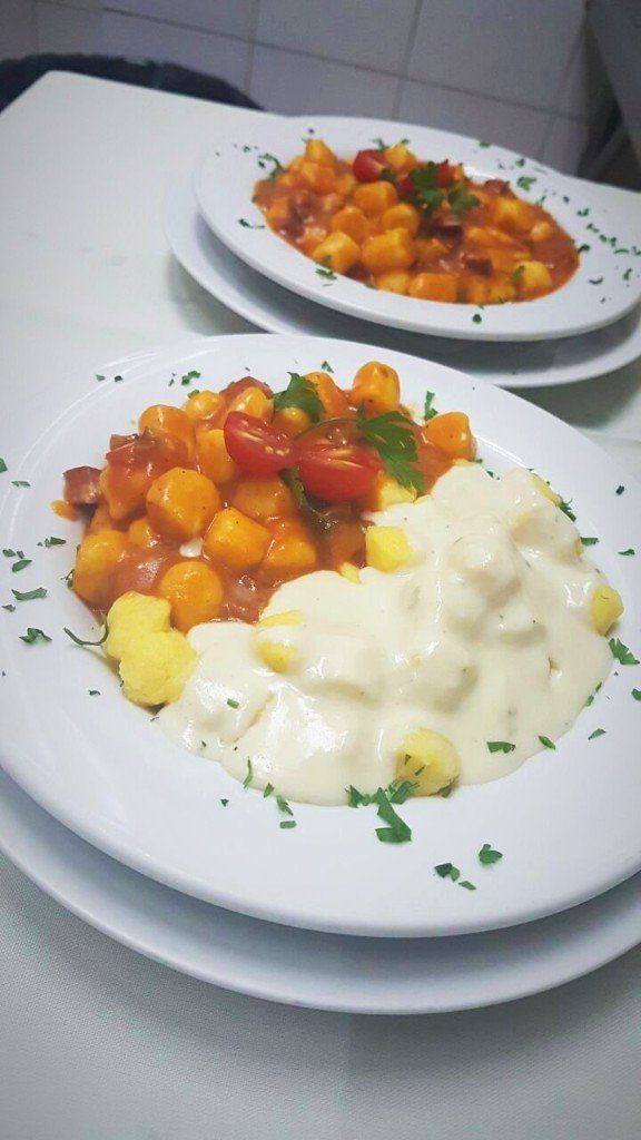 Um prato branco coberto com nhoque e molho sobre uma mesa.