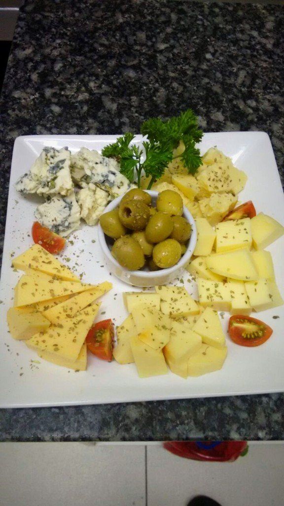 Um prato branco coberto com queijo, azeitonas, tomate e salsa.