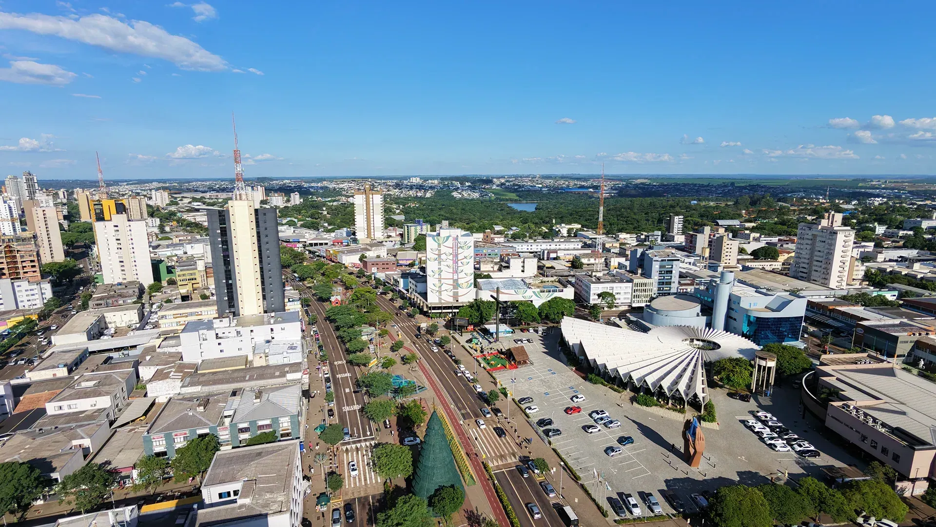Vista aérea de uma cidade com prédios altos, um amplo bulevar e um grande parque sob um céu azul.