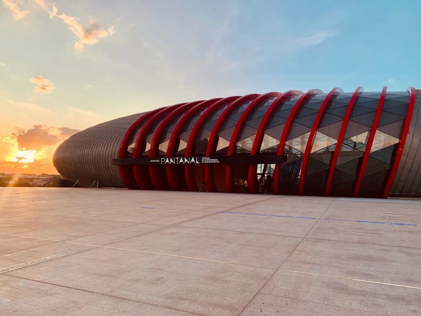 Prédio moderno em tons de vermelho e marrom com painéis de vidro. A placa diz 