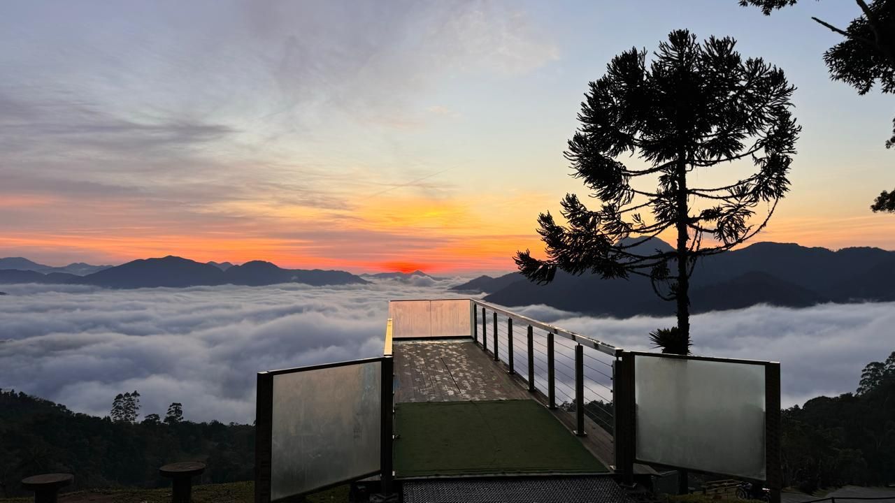 Vista da cidade ao pôr do sol, refletida em um lago tranquilo. Tons de laranja e dourado dominam o céu e a água.