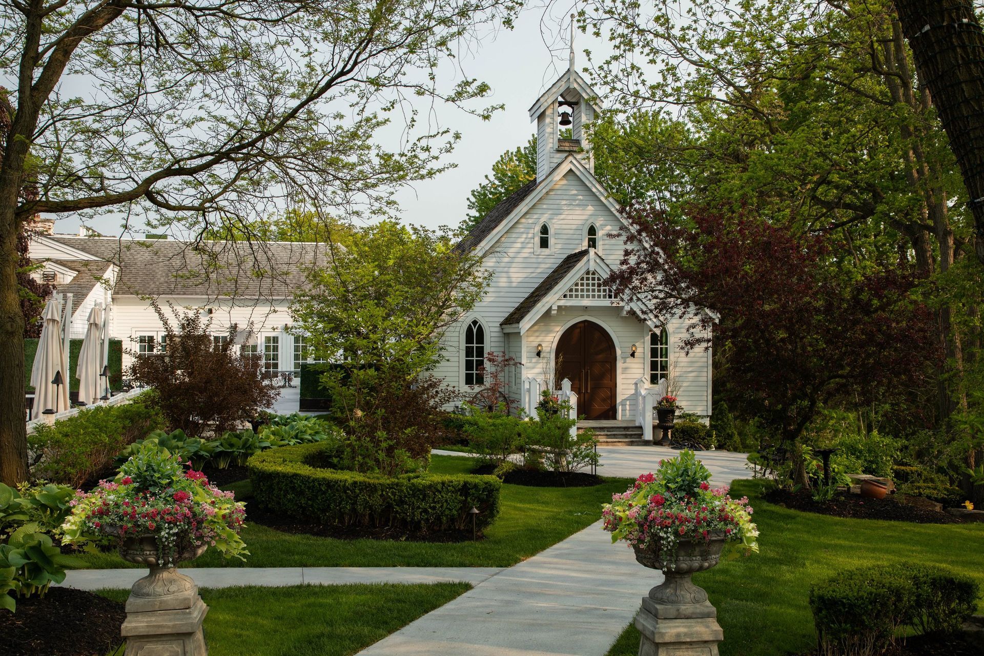 A small white church is surrounded by trees and bushes.