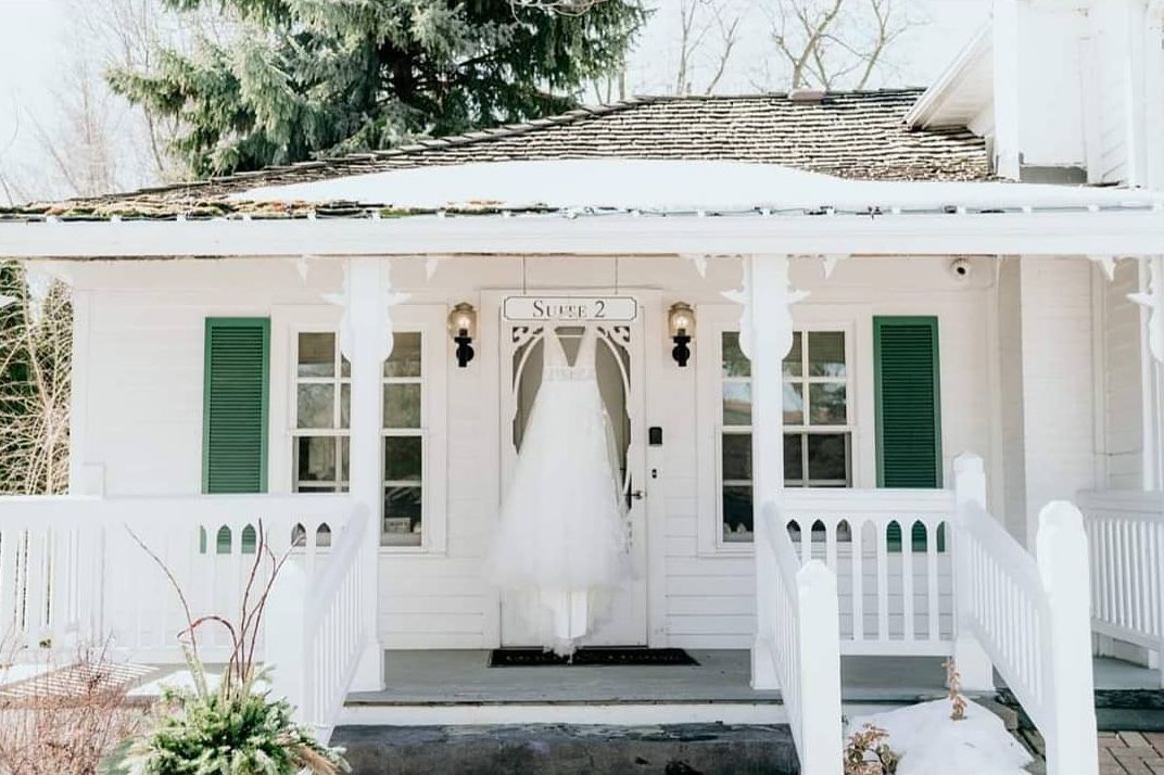 A wedding dress is hanging on the door of a white house.