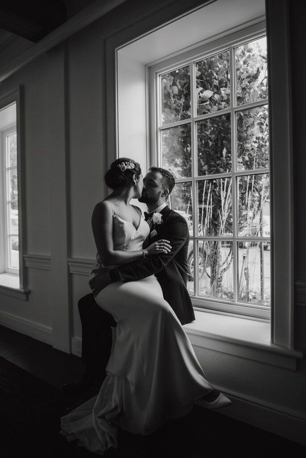 A bride and groom are kissing in front of a window.