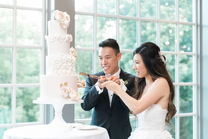 A bride and groom are cutting their wedding cake in front of a window.