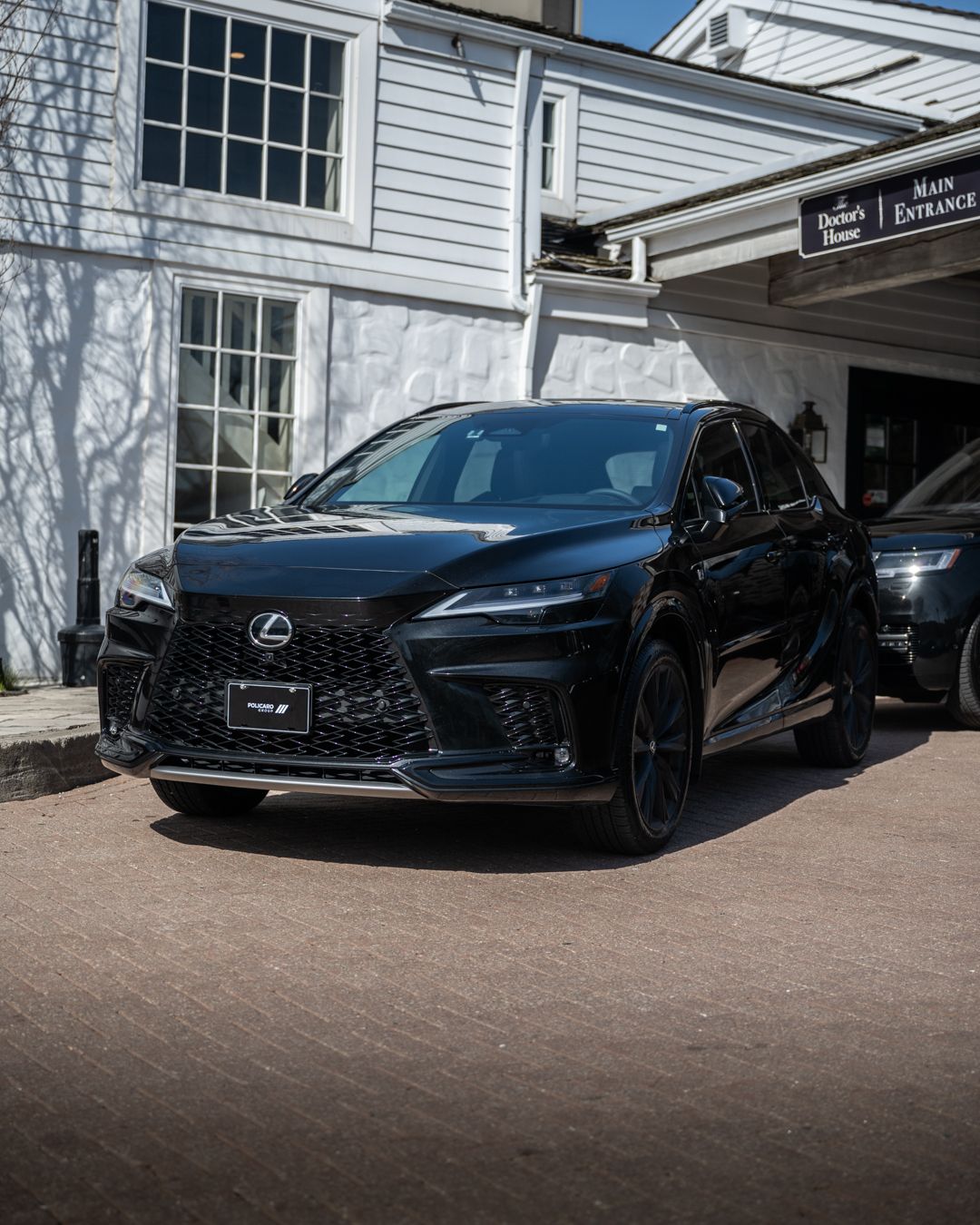 A black lexus is parked in front of a white house.