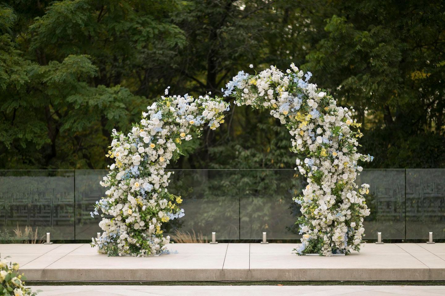 A wedding arch made of white flowers is sitting on a concrete surface.