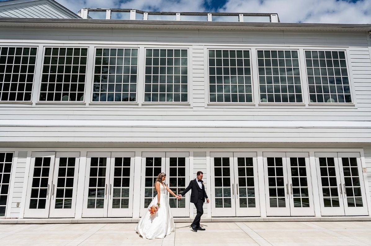 A bride and groom are walking in front of a large white building.