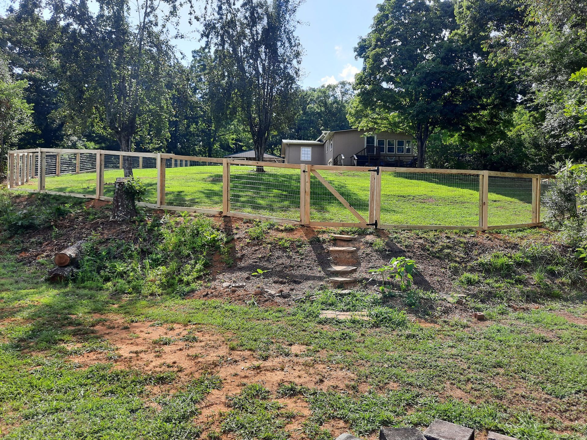A wooden fence surrounds a grassy hill with a house in the background.