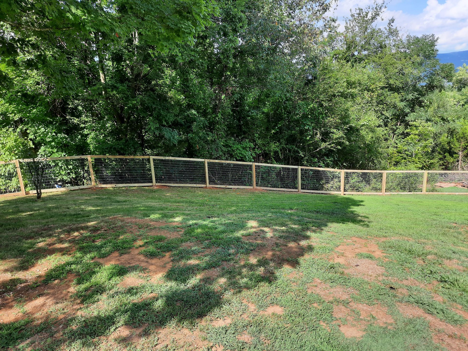 A wooden fence surrounds a lush green field with trees in the background.