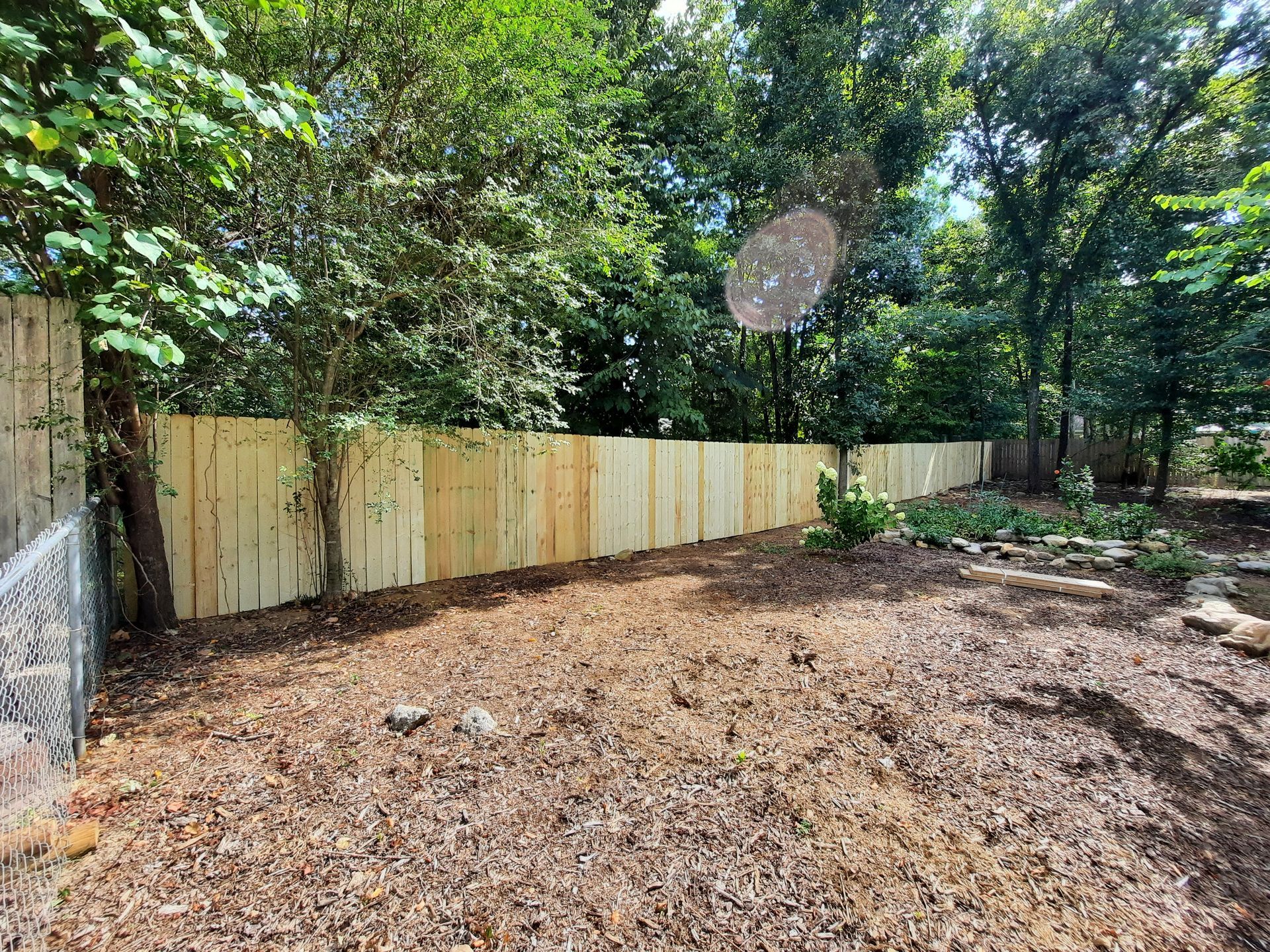 There is a wooden fence in the backyard surrounded by trees.