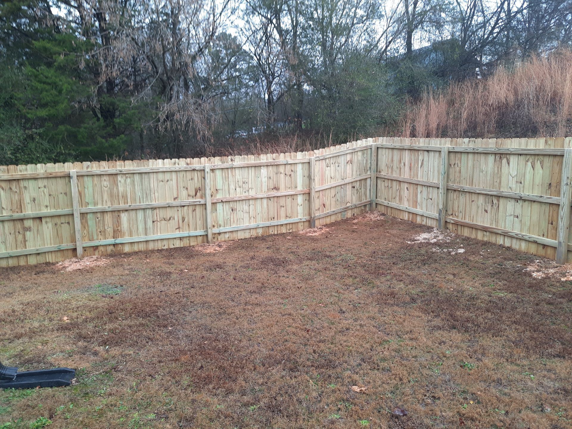 A wooden fence is in the middle of a dirt field.
