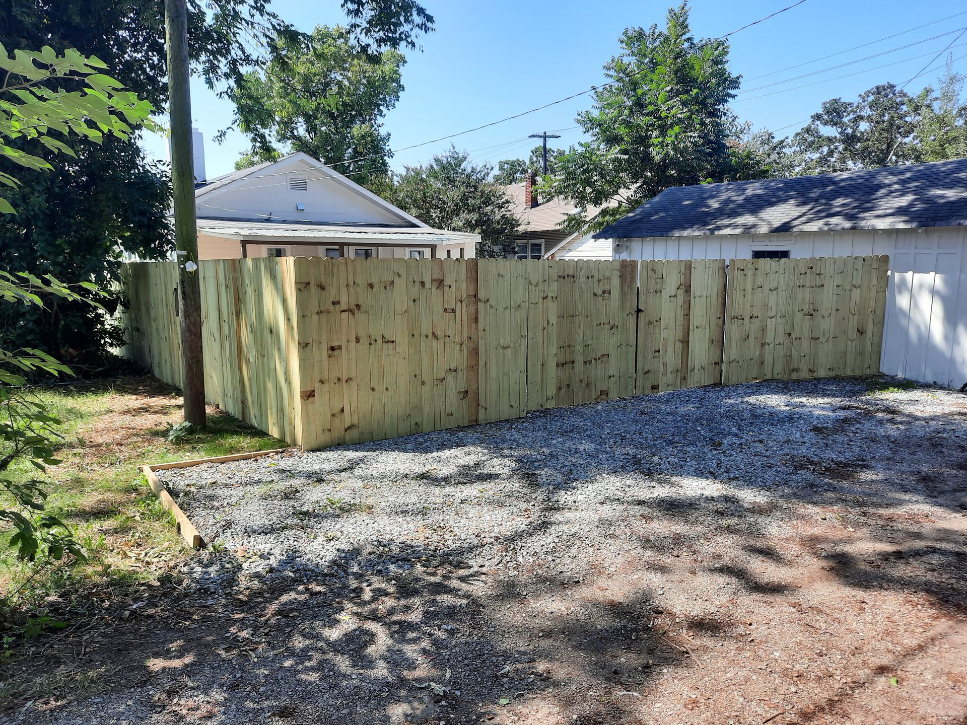 A wooden fence is surrounding a gravel driveway in front of a house.