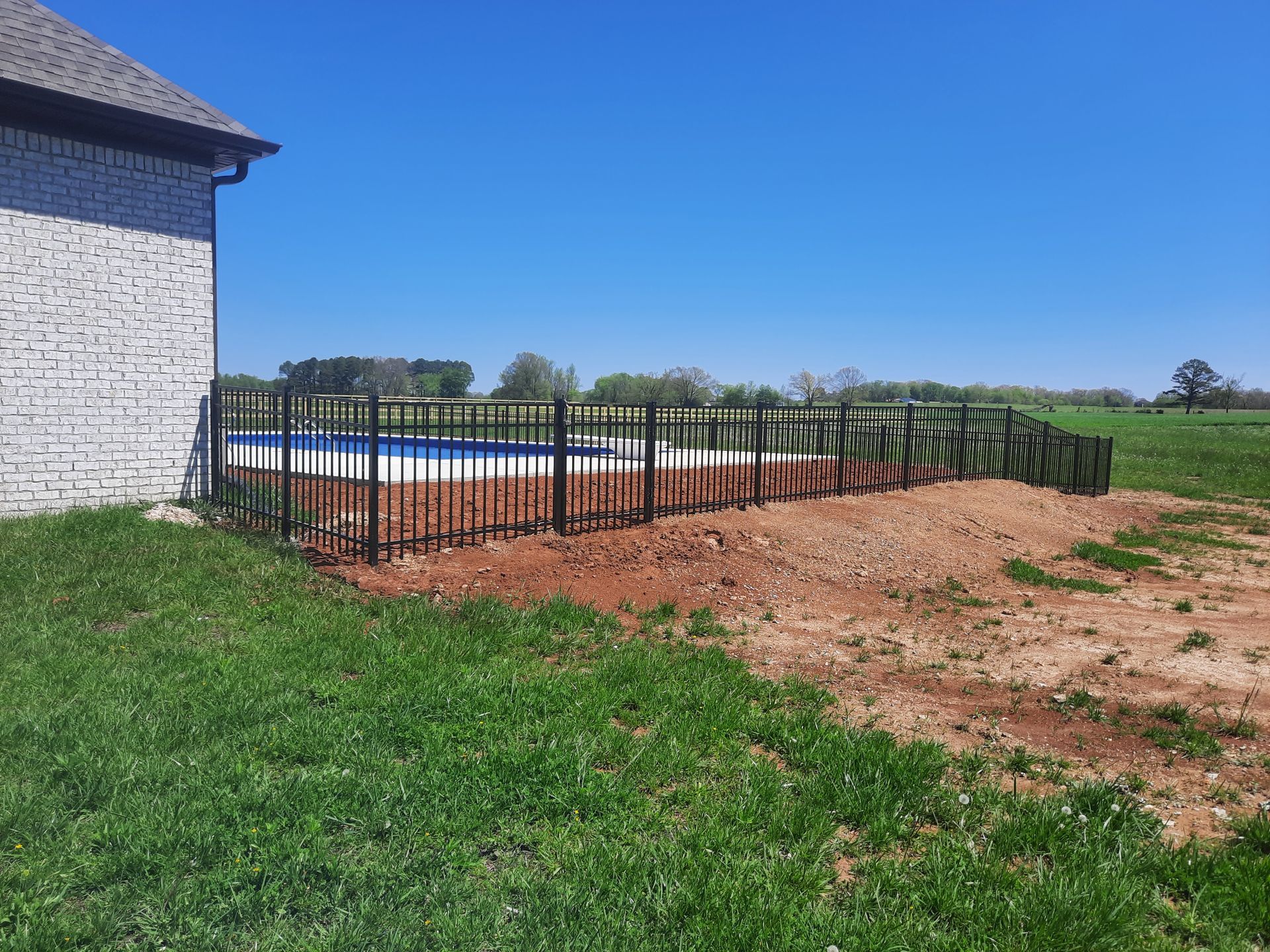 A fence surrounds a swimming pool in the backyard of a house.