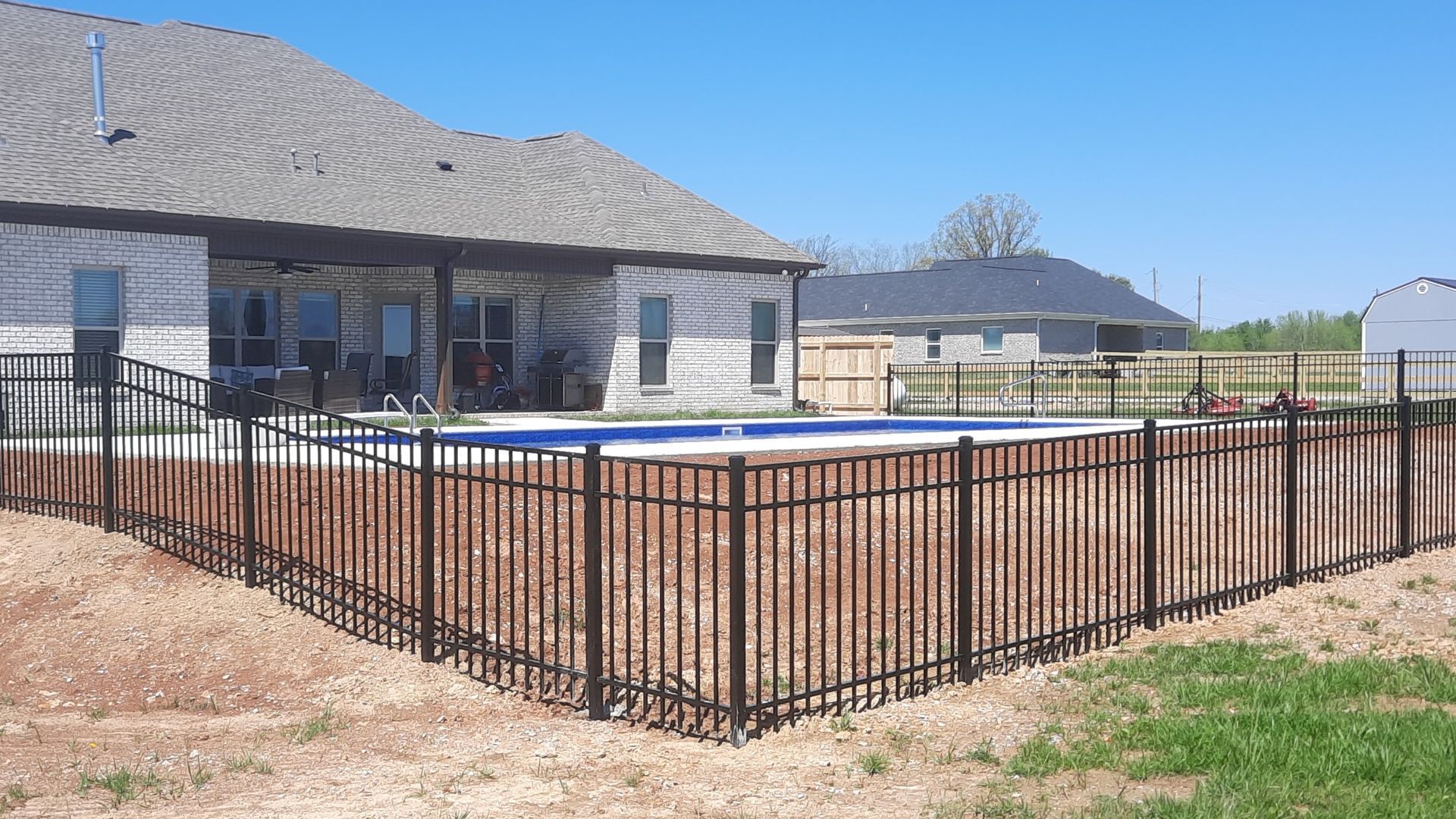 A fence surrounds a swimming pool in front of a house.