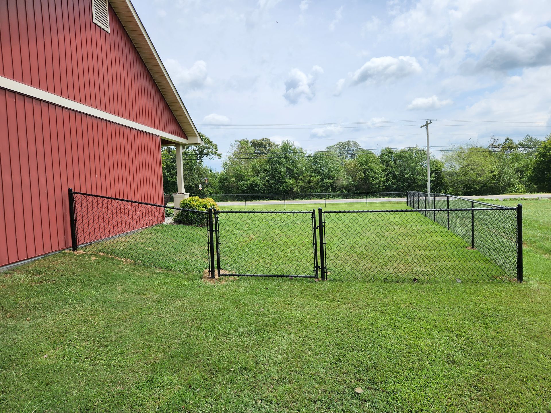 A red barn with a chain link fence and a gate in front of it.