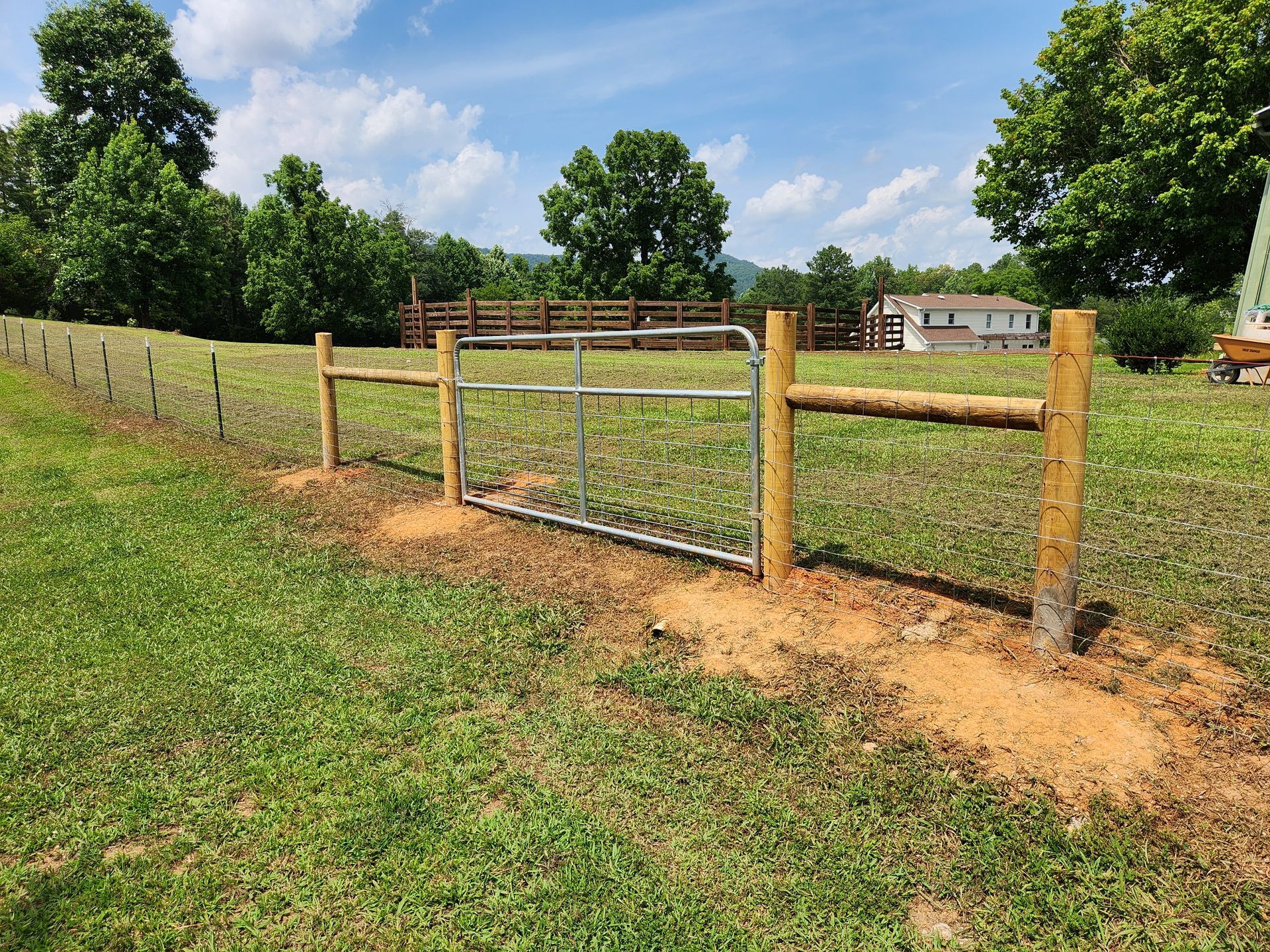 A wooden fence with a metal gate in a grassy field.