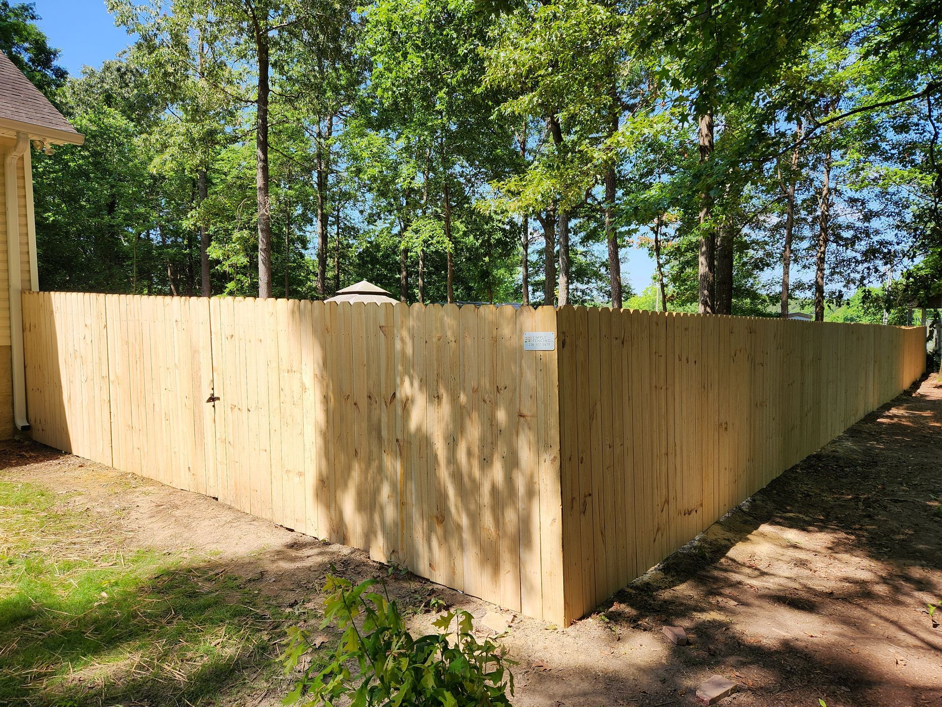 A wooden fence is surrounded by trees and a dirt road.