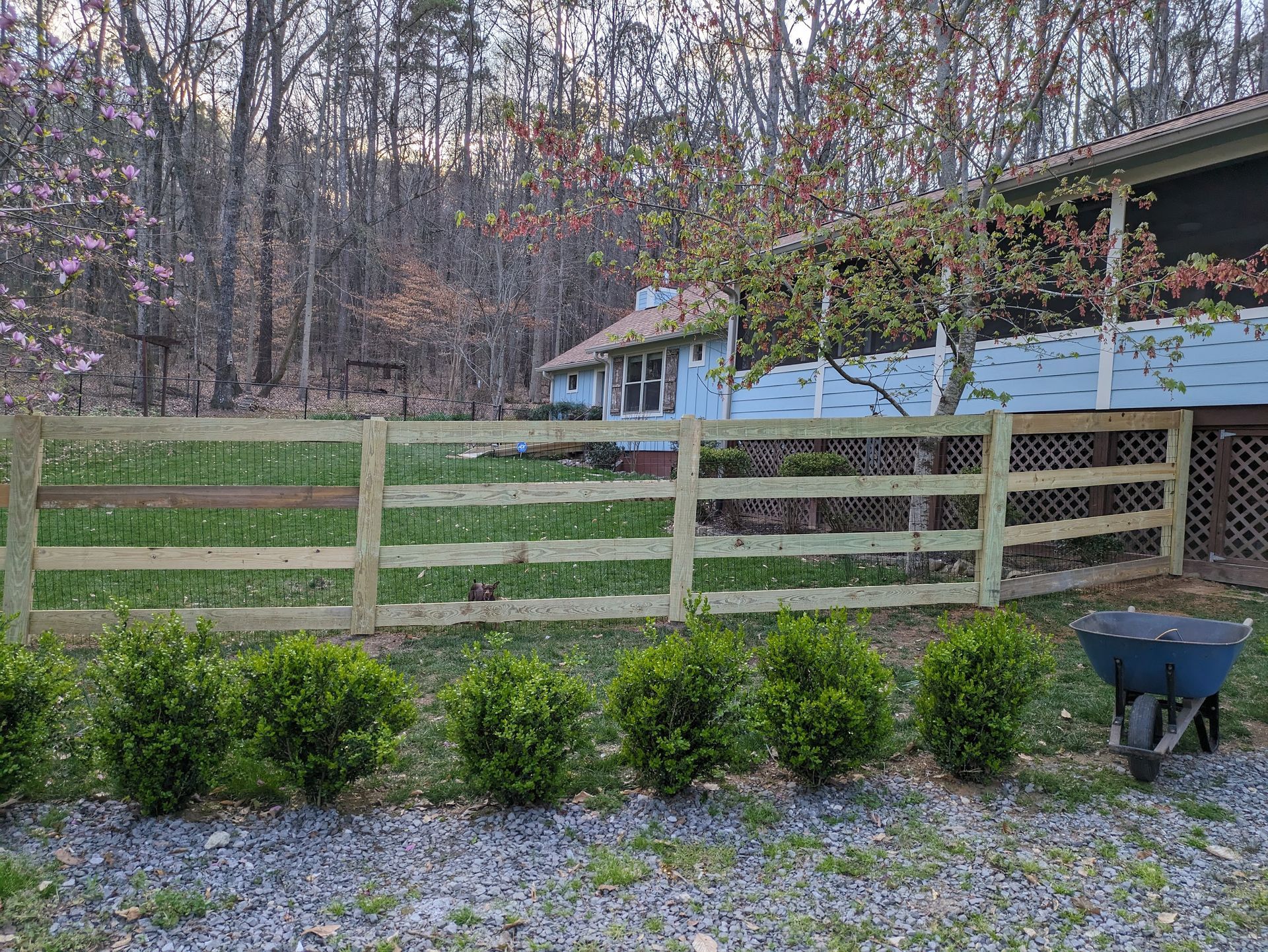 A wooden fence with a wheelbarrow in front of a house.