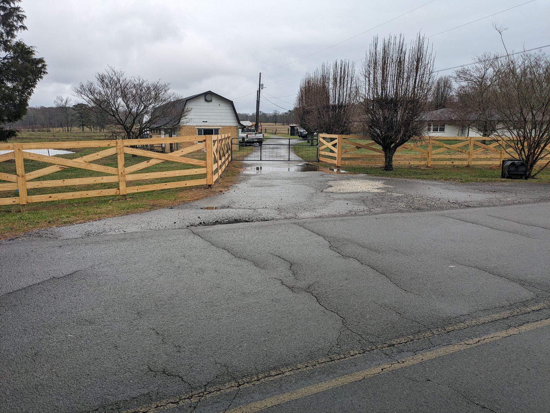 A wooden fence surrounds a driveway leading to a barn.