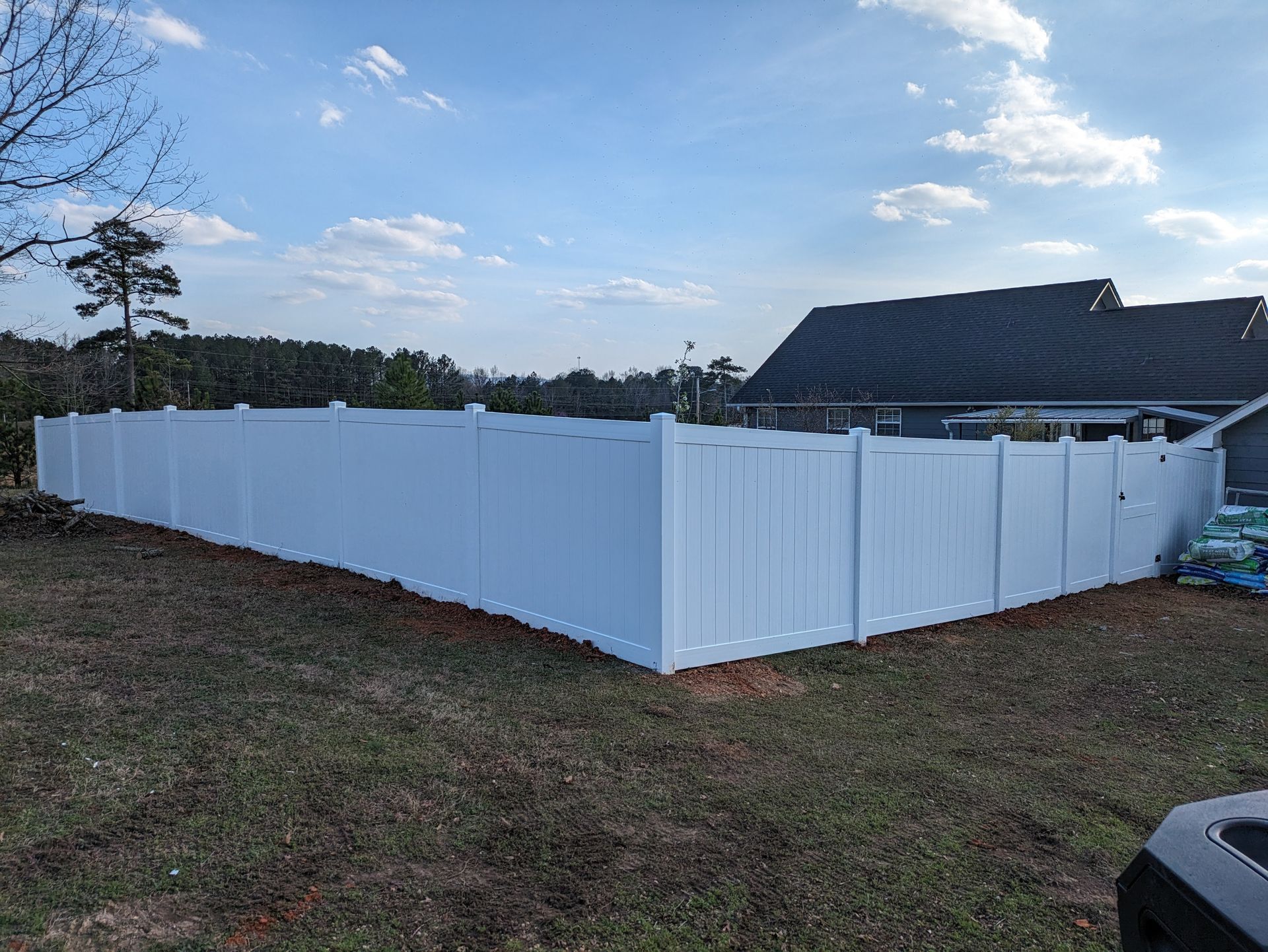 A white vinyl fence is sitting in the middle of a grassy field in front of a house.